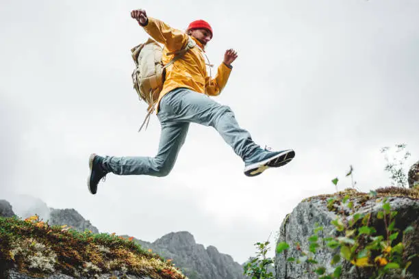 Photo of Active brave tourist jumping through cliff in mountain lifestyle outdoor journey. Man traveler with rucksack hiking mountains wilderness