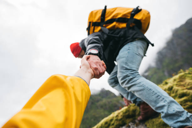 widok pov na dzielnego turystę pomagającego swojemu aktywnej przyjaciółce trzymającej się za rękę wspinając się na skałę. dwóch podróżnych wspiąć się do gór stylu życia wakacje na świeżym powietrzu - rock norway courage mountain zdjęcia i obrazy z banku zdjęć