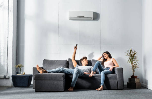 handsome boyfriend switching on air conditioner and looking at smiling girlfriend handsome boyfriend switching on air conditioner and looking at smiling girlfriend air conditioner photos stock pictures, royalty-free photos & images