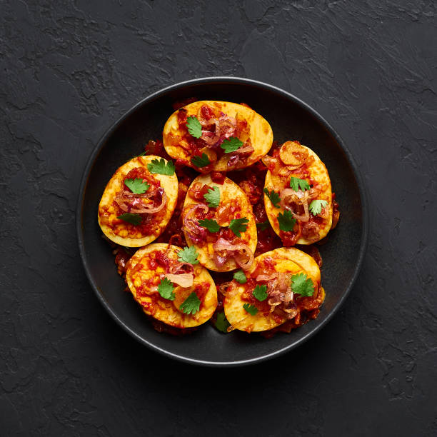 Golden Egg Curry in black bowl at dark slate background. Burmese Egg Curry is popular Myanmar Cuisine dish with duck or chicken eggs, tomatoes, ginger, onion, cilantro and spices.