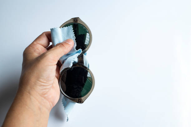istock Woman's left hand cleaning sunglasses by microfibre cleaning cloths, On white background, Close up & Macro shot, Selective focus, Optical concept 1180778562