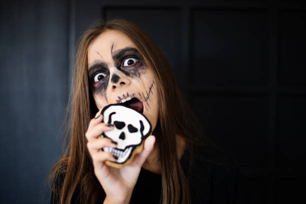 istock A girl with scary makeup eats a gingerbread skull cookie 1180778696