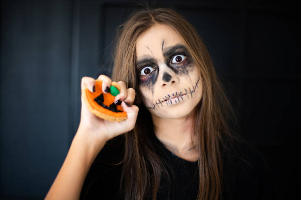 istock A girl with scary makeup breaks a gingerbread pumpkin cookie 1180778927