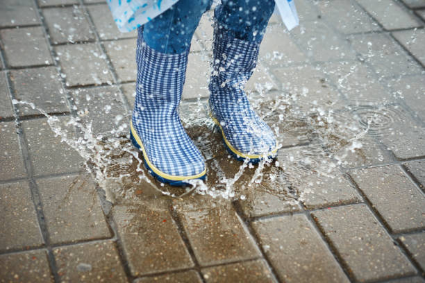 istock child in blue rubber boots jumping over the puddle in the rain 1180779492