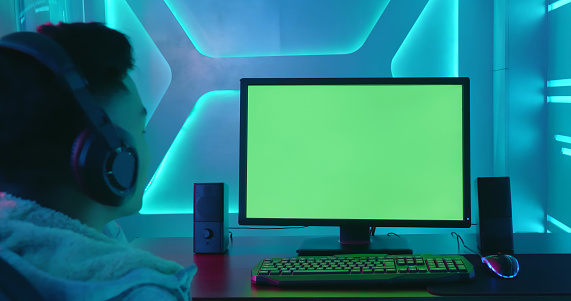 Young Asian man listen music or watch video with green chroma key screen computer