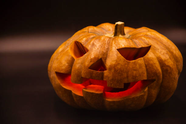 istock Pumpkin that is cut into a ghost face for Halloween, placed in a scary atmosphere, with candles shining in the dark. For use on Halloween 1180792383