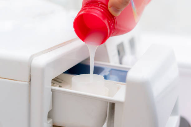 pouring the washing conditioner in the washing machine to get clean clothes pouring the washing conditioner in the washing machine to get clean clothes fabric softener photos stock pictures, royalty-free photos & images