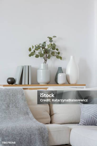 Green Flowers In Grey Vase Next To Books On Wooden Console Table In Bright Living Room Interior Stock Photo - Download Image Now