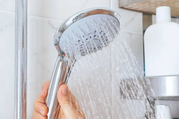 Photo of Woman hand using shower head in bathroom.
