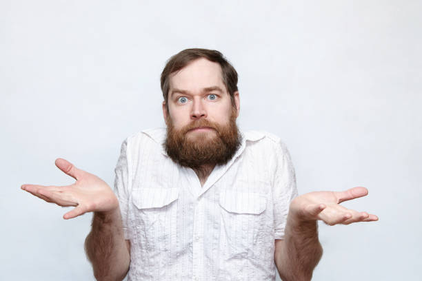 Confused man shrugging shoulders over gray background Portrait of a bearded man raising arms in confusion confusion raised eyebrows human face men stock pictures, royalty-free photos & images