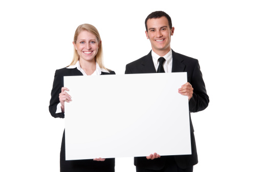 Young caucasian male and female corporate types with big smiles holding blank sign. This image has been fully retouched in Photoshop.