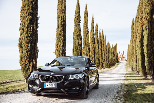 Pienza, Italy - March 12, 2017 : Brand new black coupe BMW 220d is parked at the roadside the Siena countryside along a cypress hill road.