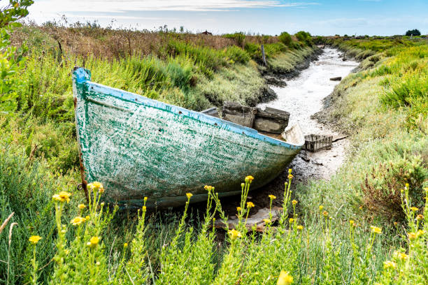The wrecks of an old wooden fishing boat are stranded on the mud at the bottom of a channel.