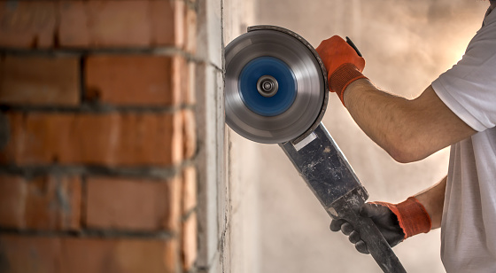 The industrial Builder works with a professional angle grinder to cut bricks and build interior walls. Professional on the construction site. The concept of electrician and handyman.
