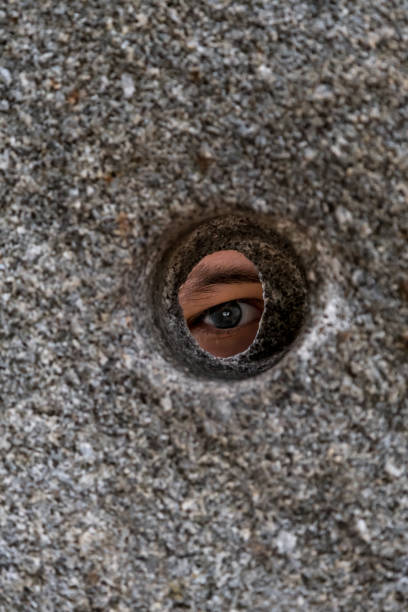 istock Open Eye Looking Through Round Hole In Stone Wall 1180814778