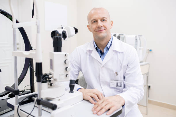 istock Happy bald mid-aged ophthalmologist in whitecoat sitting by workplace 1180815565