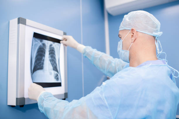 istock Experienced professional in surgical uniform and mask looking at lungs x-ray 1180815644
