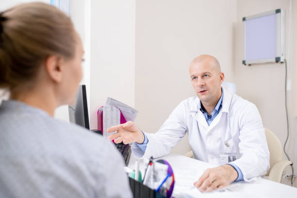 istock Confident doctor in whitecoat sitting by workplace while consulting patient 1180815673