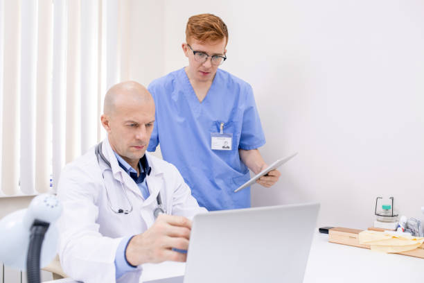 istock Mature confident doctor pointing at laptop display while making presentation 1180815702