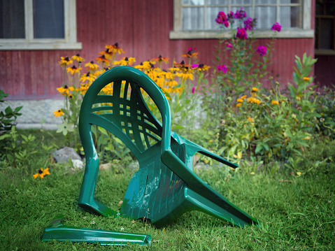 Abandoned plastic garden chair with brokedn leg, outdoor shot
