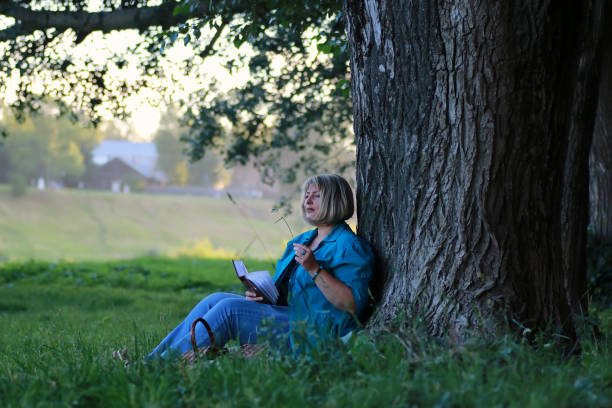 istock woman in the park tree reading book 1180828339