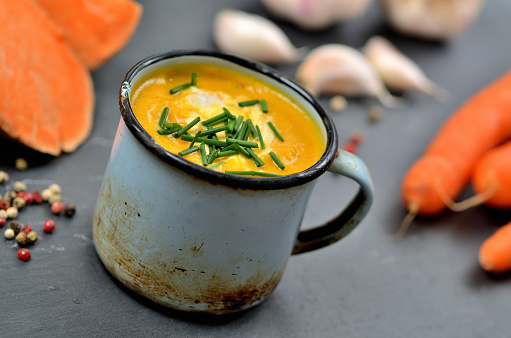Close-up of pumpkin soup with cream and fresh chive in old enamel cup.