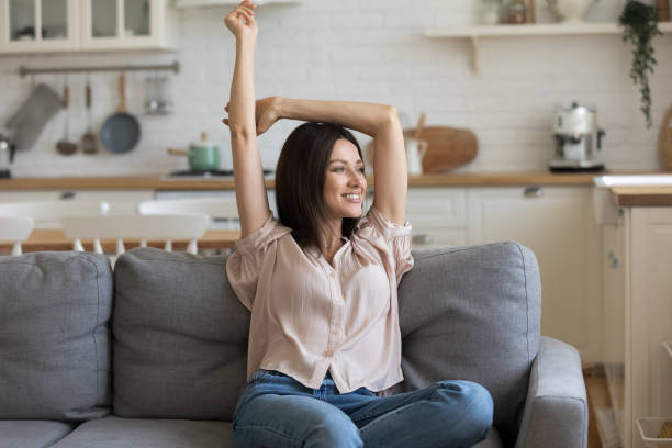 istock Smiling young woman relaxing on couch, stretching hands, looking aside 1180834975