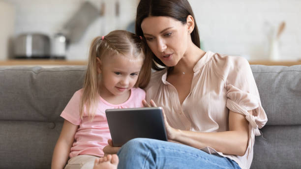 madre che insegna alla figlia piccola a usare il tablet da vicino - child digital tablet mother teaching foto e immagini stock