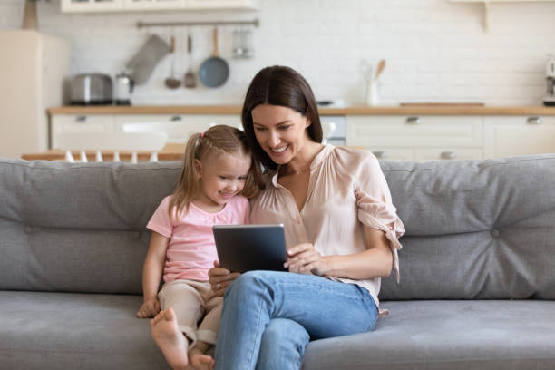 istock Happy mother and daughter using computer tablet, making video call 1180834993