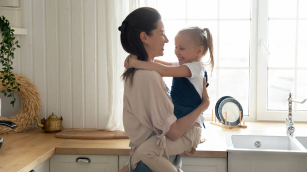 istock Happy mother holding little daughter, hugging, standing in kitchen 1180835053