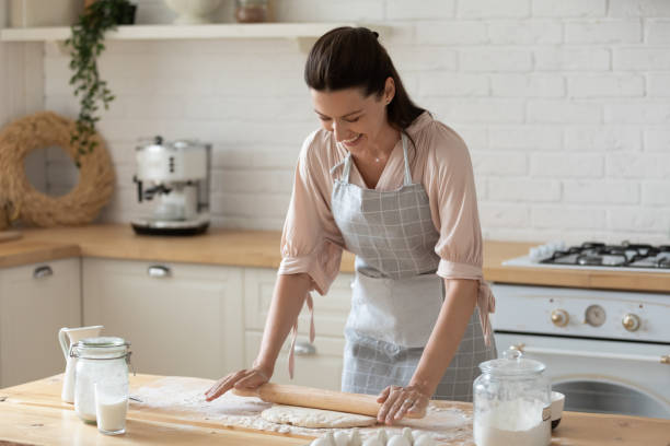 istock Smiling young woman wearing apron rolling out dough in kitchen 1180835061