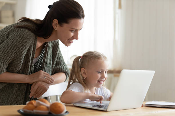 istock Smiling mother and little daughter using laptop, looking at screen 1180835068