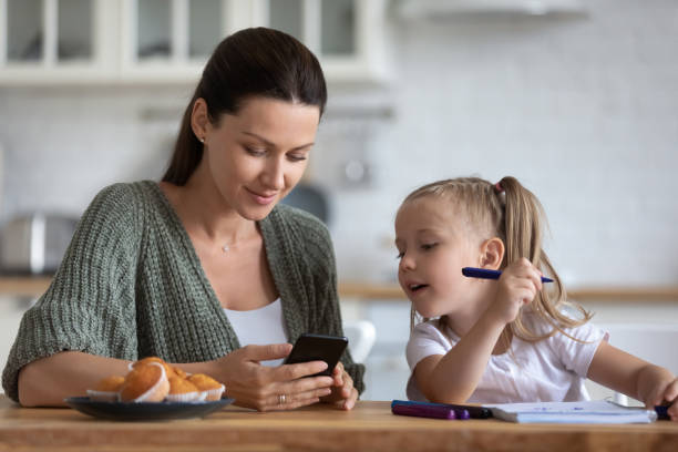 istock Little daughter distracted from drawing, looking at phone with mother 1180835072