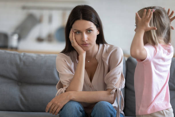 Unhappy mother having problem with noisy naughty little daughter Unhappy mother having problem with noisy naughty little daughter screaming, demanding attention, child tantrum manipulation concept, tired thoughtful mum holding head, sitting on couch at home child behaving badly stock pictures, royalty-free photos & images