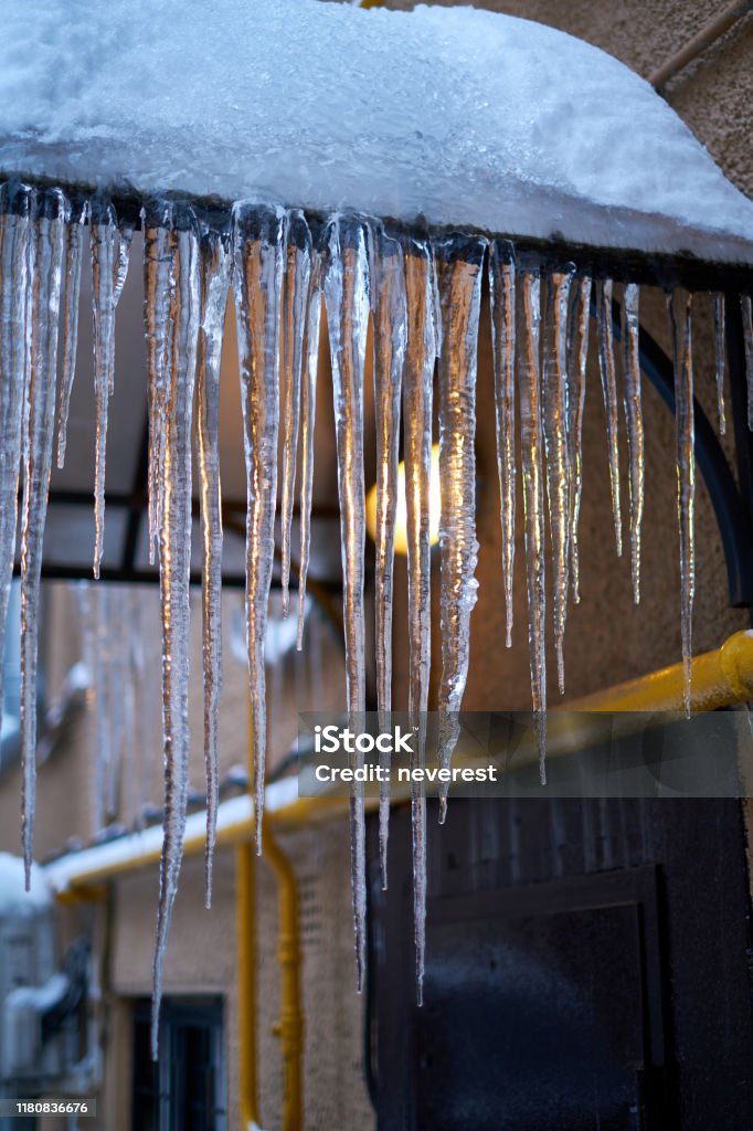 Backlit icicles on a roof Long sharp transparent icicles on a brim of a snow covered roof Climate Stock Photo