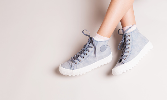 Pastel blue sneakers on crossed legs. Footwear on grey background. Layout with free copy (text) space.