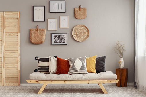 Cozy retro-chic interior with a green velvet armchair and a low white and hardwood cabinet in front of a pastel powder pink plaster wall background with copy space. A low coffee table with ceramic containers, vases on the white hardwood floor, birdcage lamps, and decoration (lush foliage: monstera, banana/palm tree, pillow) with 2 hardwood slat doors on each side. The 50s- 60s decoration, art deco style. A slight vintage effect was added. 3D rendered image.