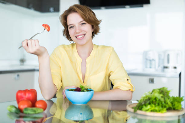 istock Smiling young woman eating fresh salad in modern kitchen 1180841044