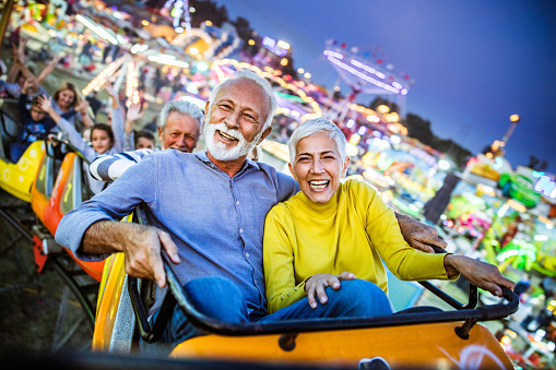 Happy senior couple having fun while riding on rollercoaster at amusement park.