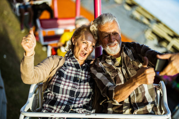 istock Happy senior couple having fun while taking a selfie during amusement park ride. 1180842757