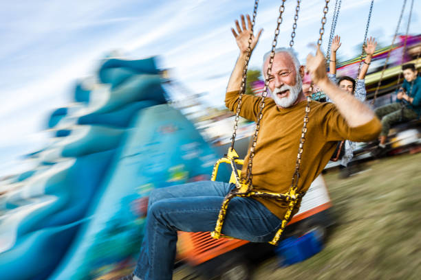 istock Happy mature man on a chain swing ride at amusement park in blurred motion. 1180844032