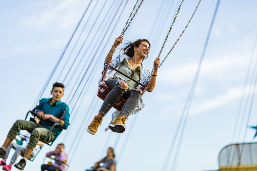 Low angle view of carefree woman having fun while riding on chain swing at amusement park. There are people in the background.