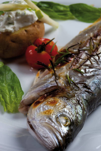 delicious baked sea bass grilled with special sauce and cherry tomatoes. traditional turkish cuisine and fish dishes concept. vertical close-up detail shot. - sea bass prepared fish food grilled imagens e fotografias de stock
