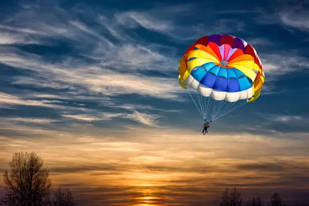 Photo of People are gliding with a parachute on the background of sunset.