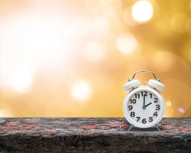 Photo of Daylight saving time end concept with alarm clock on orange autumn blur background
