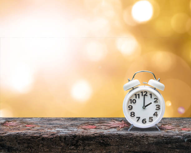 daylight saving time end concept with alarm clock on orange autumn blur background - clock time alarm clock orange imagens e fotografias de stock