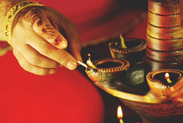 horizontal photograph of indian festival diwali deepawali being celebrated, a lady, woman with henna or mehndi and a big gold kangan lighting mitti or terracotta diya with matchstick - fire match women flame imagens e fotografias de stock