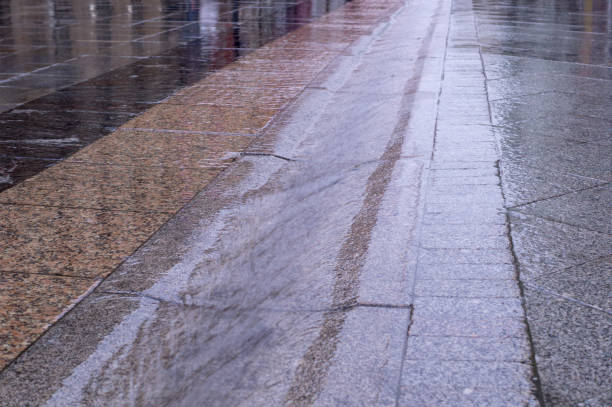 istock street gutter with water flow on tiled sidewalk at rainy day. background, weather. 1180886303