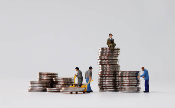 Miniature people carrying coins in a cart and a miniature man sitting on a coin. stock photo