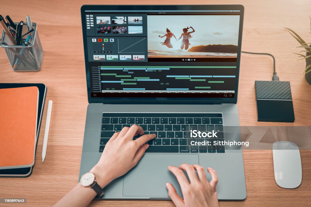 Concept of simple operation of blogger and vlogger, hand using laptop on video editor works with footage on wooden table, camera and accessories on table. Editor Stock Photo